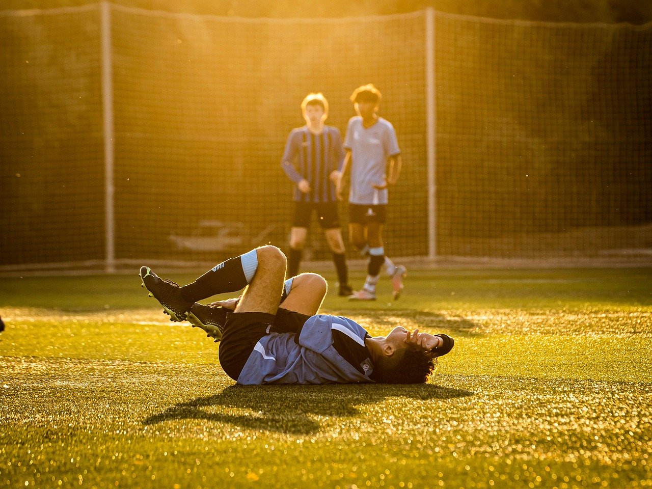 Football player lying on the ground in pain after a tackle, a common example relevant to Sports Injury Claims in the UK.