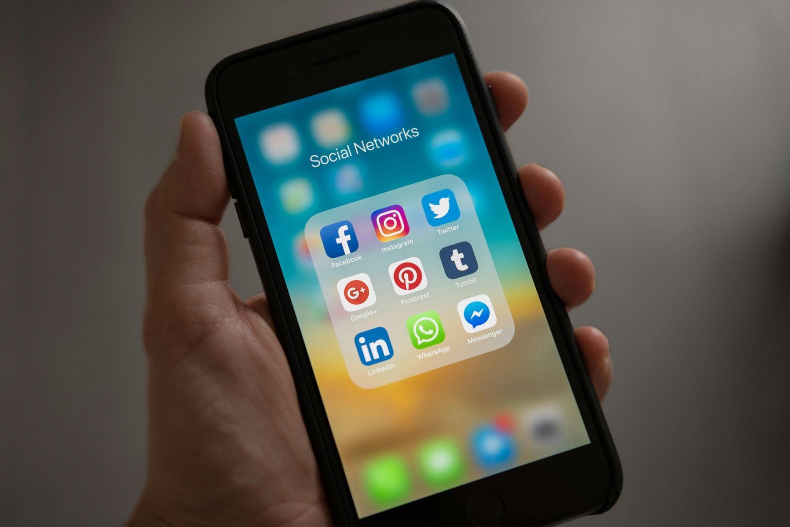 Person holding a smartphone showing various social media applications against a dark background.